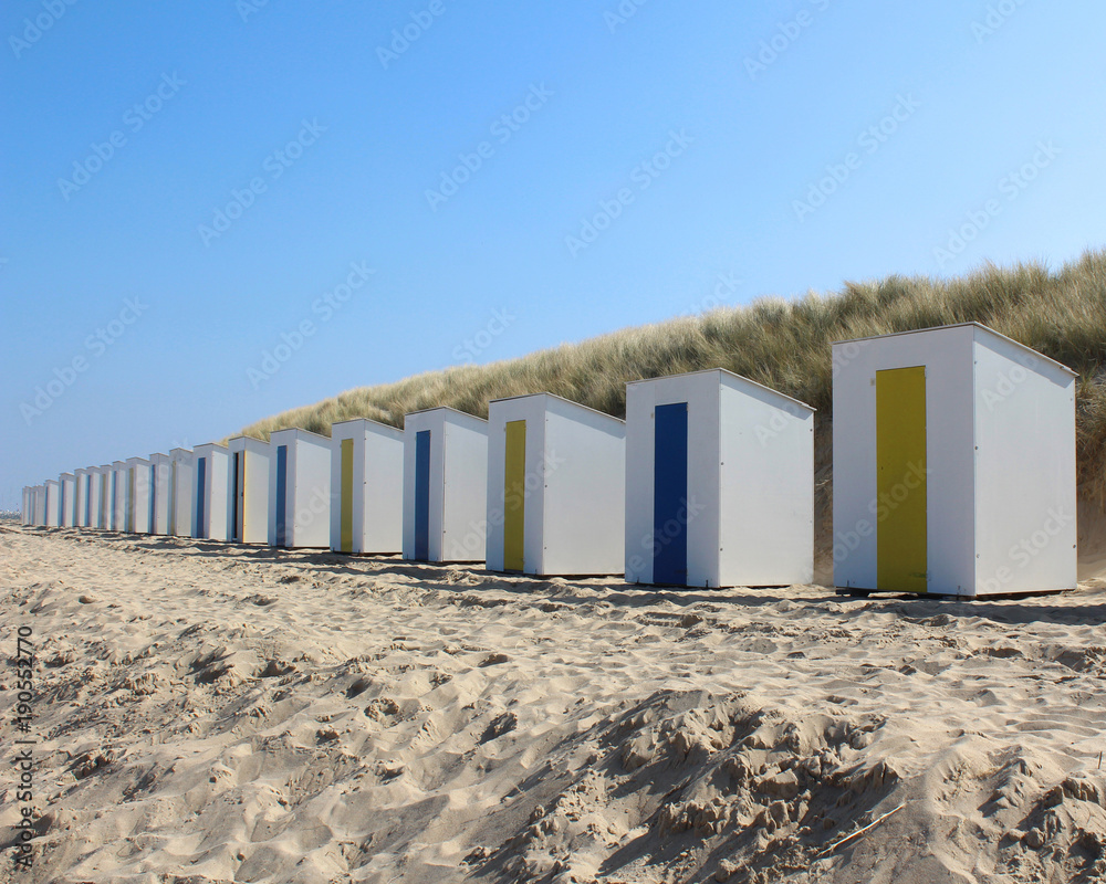 A row of identical beach huts on a sandy beach at Cadzand Bad in Zeeuws-Vlaanderen in the far south west of the Netherlands.