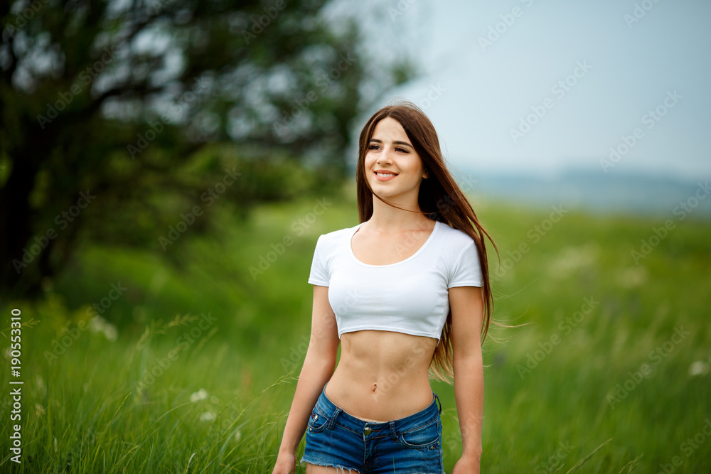 Beautiful woman walking in the summer rural meadow. Young lady in green field. Outdoor portrait of a beautiful woman Beautiful woman walking in the summer rural meadow. Young lady in green field. Outdoor portrait of a beautiful woman