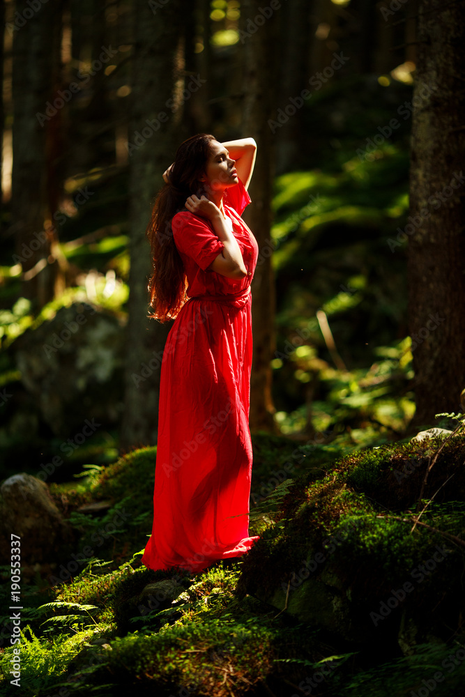 Portrait of romantic woman in fairy forest. Young woman in red dress standing in the woods