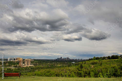  View of downtown Calgary from Edworthy park, early spring, cloudy sky, bench in the foreground