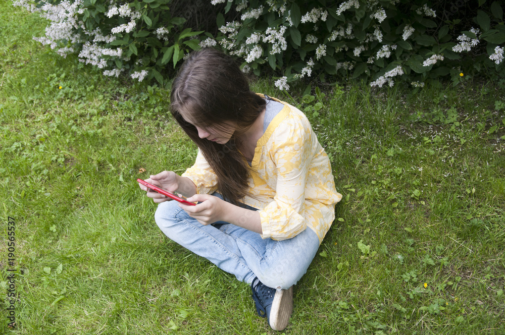 Fototapeta premium Beautiful teenager girl with tablet computer sits on the grass in Park. Photo