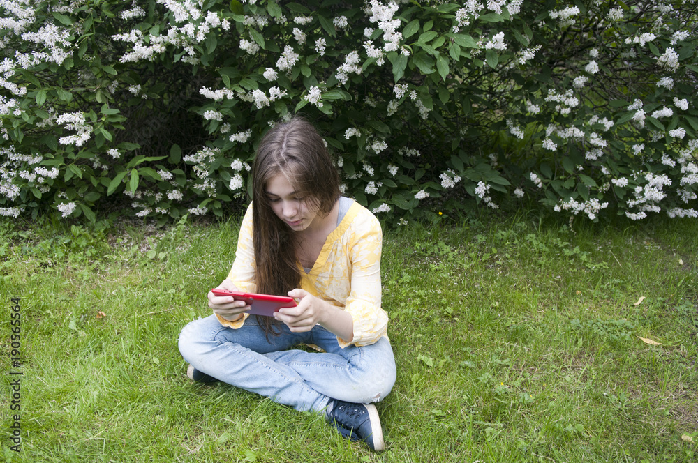 Beautiful teenager girl with tablet computer sits on the grass in Park. Photo