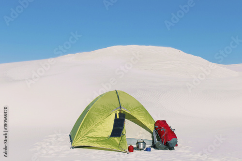 Journey through the desert with a backpack and tent. The tent is on a sandy crest.