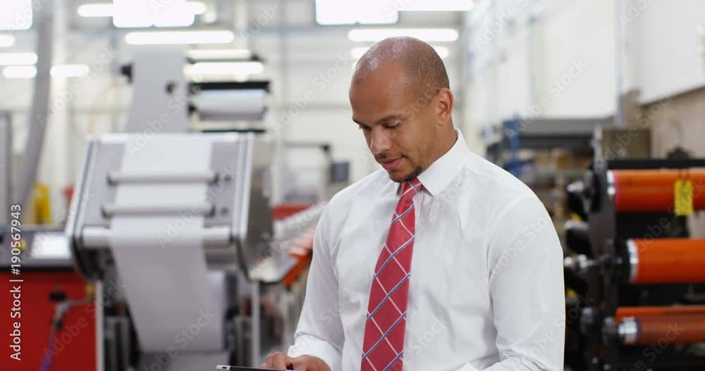 4K Business manager in print factory working on computer tablet. Crane shot panning upwards offering interesting change of background. 4K Business manager in print factory working on computer tablet. Crane shot panning upwards offering interesting change of background.