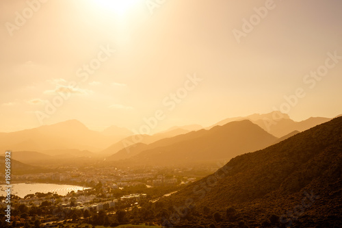 View of Port de Pollenca, Mallorca. Top view of the town. The sun setting in the mountains, haze. Silhouette of hills. Gulf town. photo