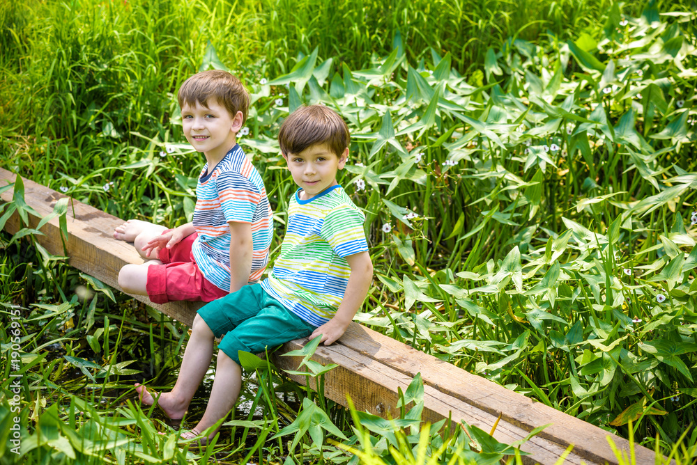 Two cute little boys sitting on a wooden bridge Two cute little boys sitting on a wooden bridge