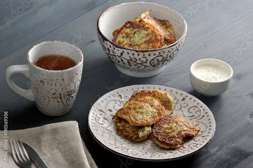 fritters of zucchini with dill in a deep dish, tea, sour cream