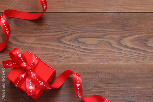 Gift red box with a ribbon on a wooden table