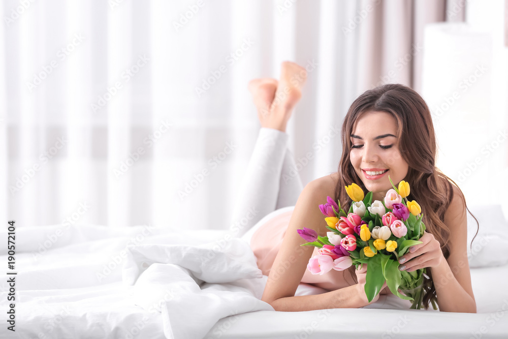 Beautiful woman with bouquet of tulips on bed at home Beautiful woman with bouquet of tulips on bed at home