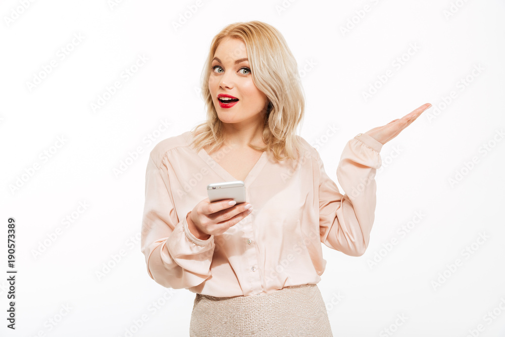 Portrait of charming blonde woman holding smartphone and gesturing hand aside, isolated over white background copy space Portrait of charming blonde woman holding smartphone and gesturing hand aside, isolated over white background copy space