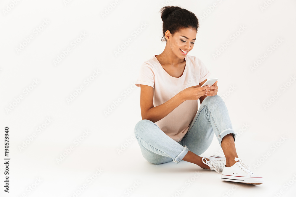 Portrait of afro american woman in casual sitting on floor with legs crossed and using mobile phone, isolated over white background Portrait of afro american woman in casual sitting on floor with legs crossed and using mobile phone, isolated over white background