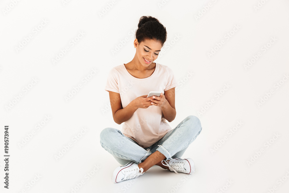 Portrait of woman in casual sitting on floor with legs crossed and using mobile phone, isolated over white background Portrait of woman in casual sitting on floor with legs crossed and using mobile phone, isolated over white background