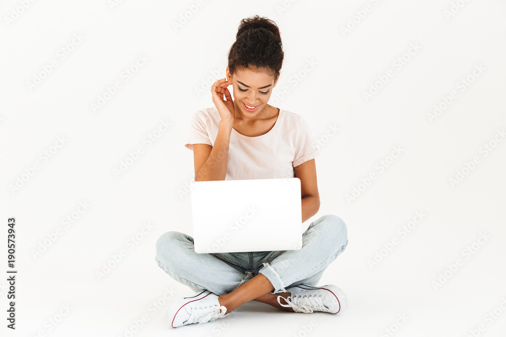 Portrait of mixed race woman in casual sitting on floor in lotus pose and working on notebook, isolated over white background Portrait of mixed race woman in casual sitting on floor in lotus pose and working on notebook, isolated over white background
