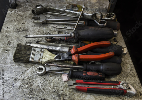 An untidy workbench full of greasy old tools set for repairing or maintenance hanging or laying on a bench in a garage