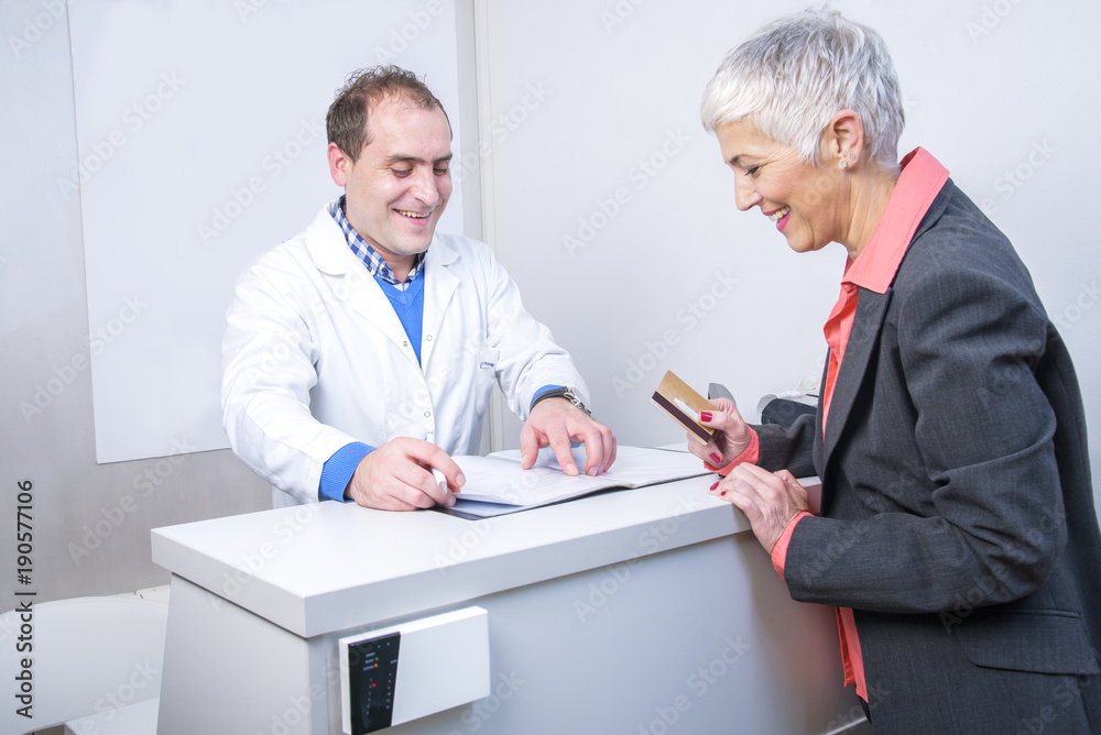 Obraz premium Senior woman paying her medical bill at the clinic with her credit card