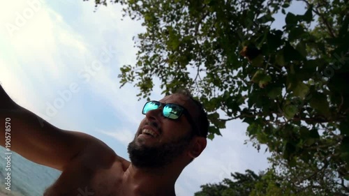 Happy young man taking selfie, video during swinging on the beach, slow motion
