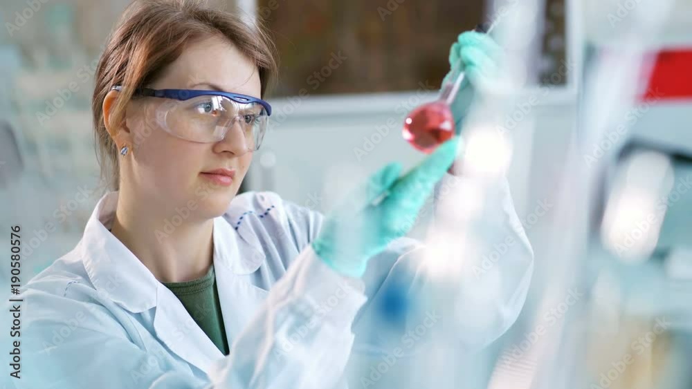 Young female scientist checking test tubes in the lab. Woman wears protective goggles