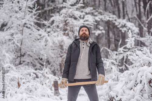 Bearded man with axe in snowy forest. photo