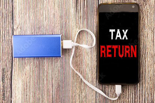 Word, writing Tax Return. Business concept for Accounting Money Return written on mobile cell phone mobile and power-bank charger on old wood wooden background photo