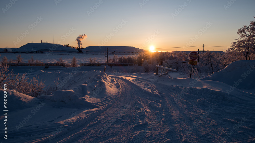 Arctic landscape and industry. At 1:25 pm at sunset in the Far North. Railway in the front and iron ore mines with smoking chimney on the horizon. This scenery close to Kiruna in Swedish Lapland.