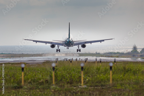 Airplane is landing at airport, sea and runway lights on background, copy space, back view/ Landing aircraft low over the runway, day light/ Vacation, travel and aviation concept