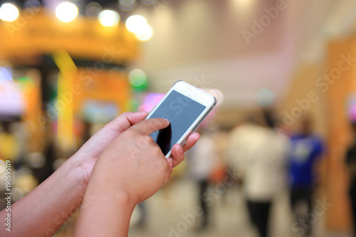 hand hold and touch screen smart phone, on abstract blurred image of trade show for background.