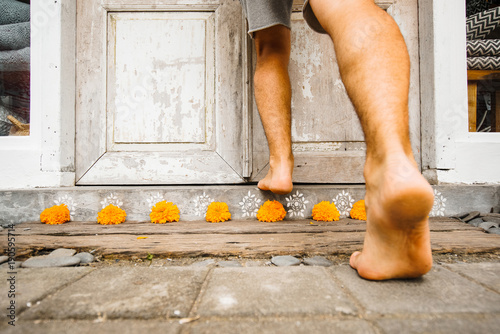 Male bare feet enter the house stepping over the threshold with flowers. The traditional entrance to the house of Asia is decorated with orange flowers. photo