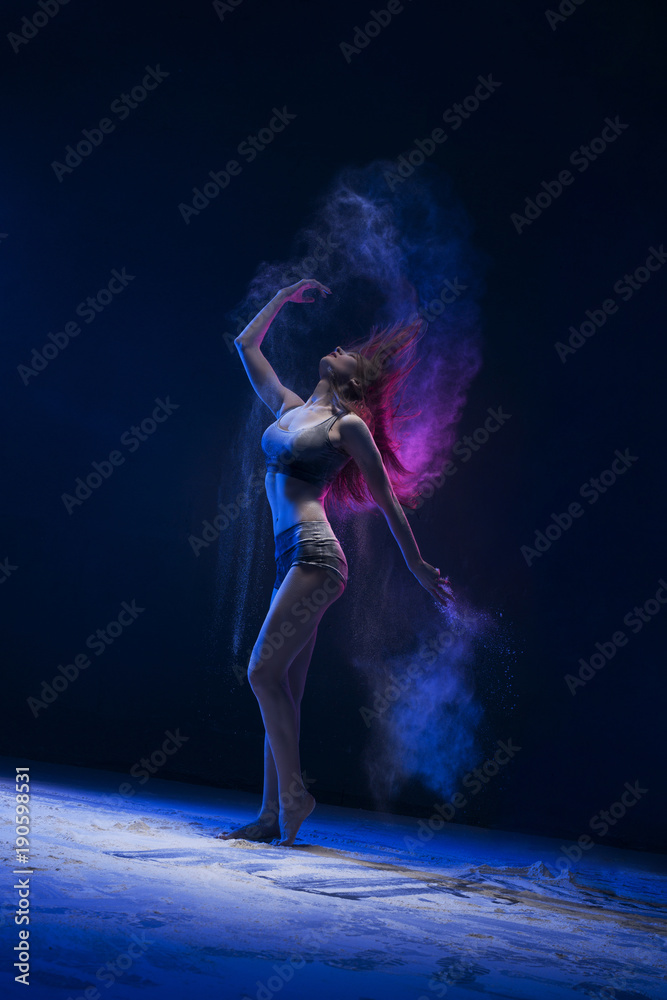 Slim girl dancing in blue dust cloud profile view