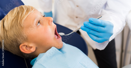 Young doctor in white is taking examination of a boy on the chair