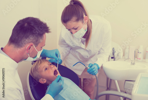 Stomatologist man with woman assistant are diagnosticating to young patient which is sitting