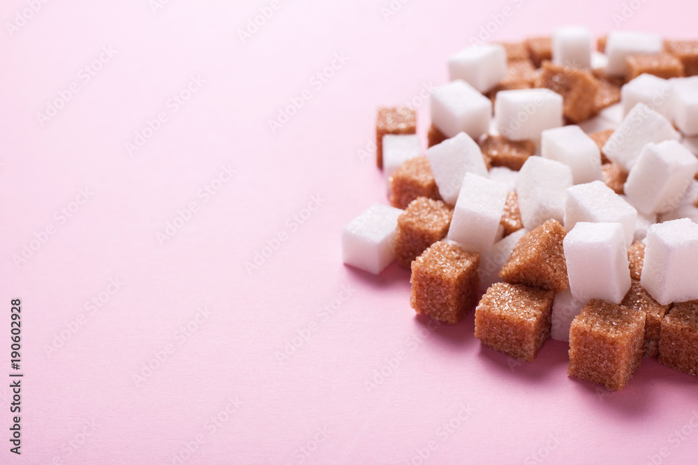 White and brown cane sugar cubes pile on a pink background. Copy space for text