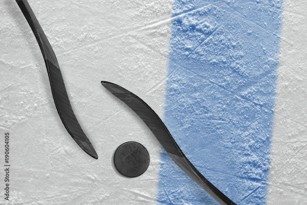 Fototapeta premium Two hockey sticks, a puck and a fragment of the ice arena with a blue line