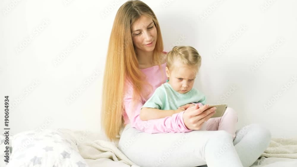 Happy young mother and daughter playing, drawing, playing games on your smartphone braid braids, read. Happy young mother and daughter playing, drawing, playing games on your smartphone braid braids, read.