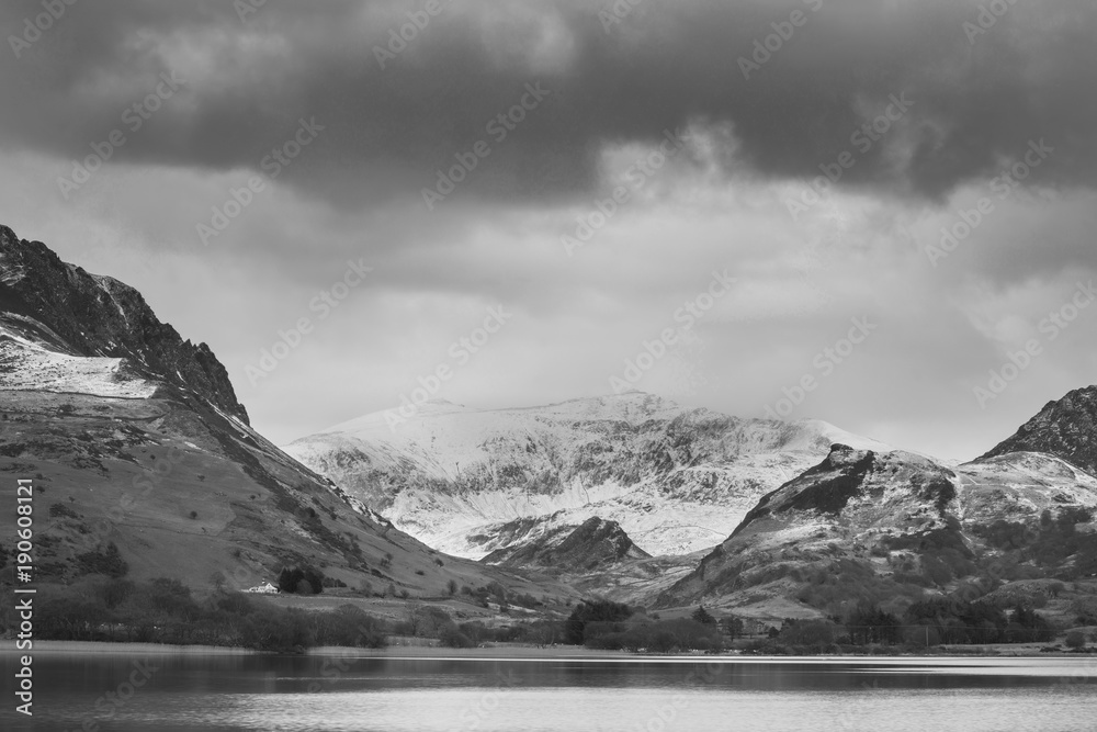 Beautiful  black and white Winter landscape image of Llyn Nantlle in Snowdonia National Park with snow capped mountains in background