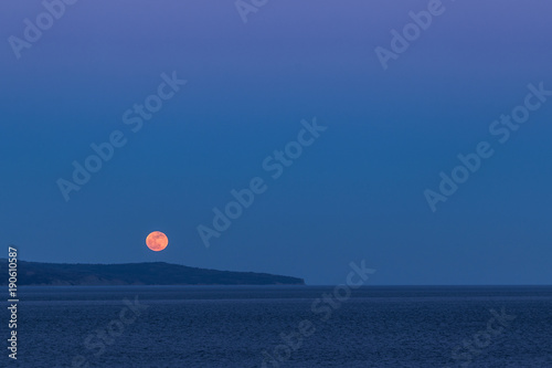 Full blood-red moon rising over the seashore