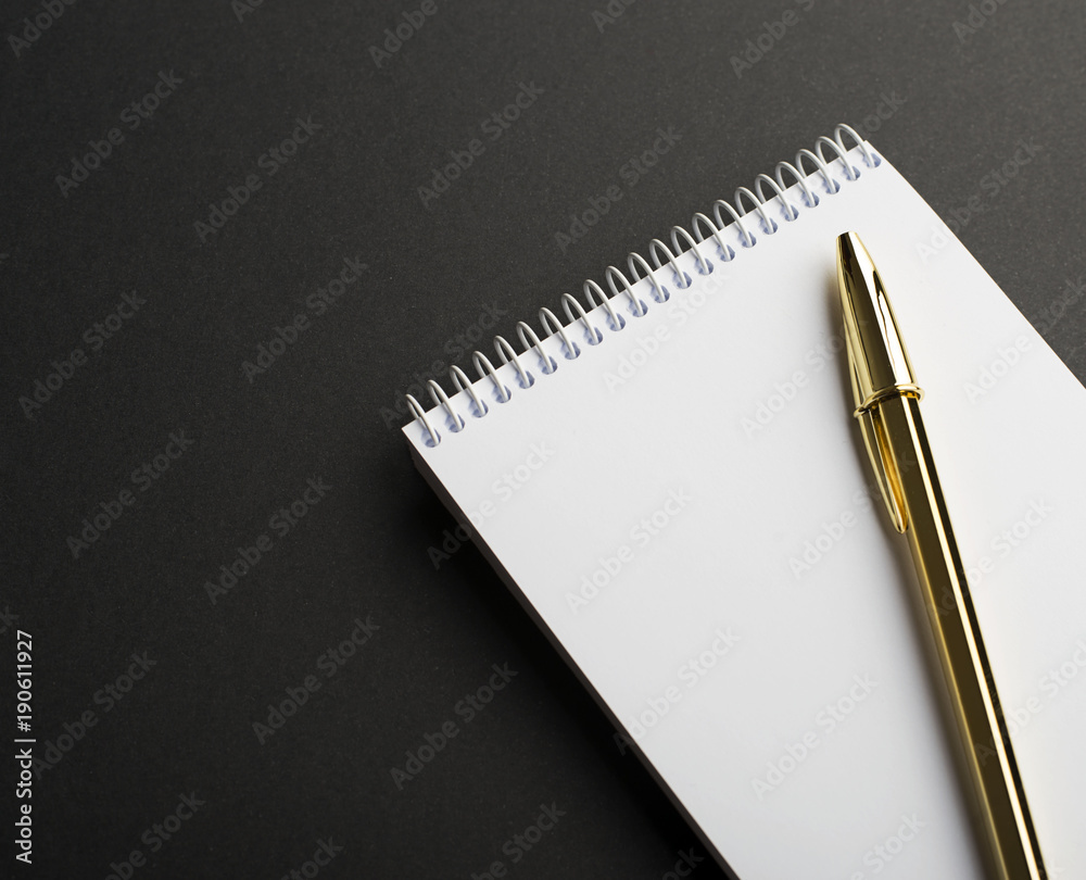 Golden ballpoint pen on notepad with empty page, on black background. Copy space. Mockup. Golden ballpoint pen on notepad with empty page, on black background. Copy space. Mockup.