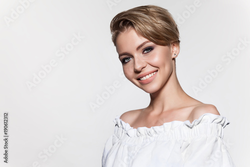 Young beautiful woman with stylish short haircut, studio portrait. Attractive model smiling and looks at camera. Portrait of cute girl with fresh make-up, isolated on white background.
