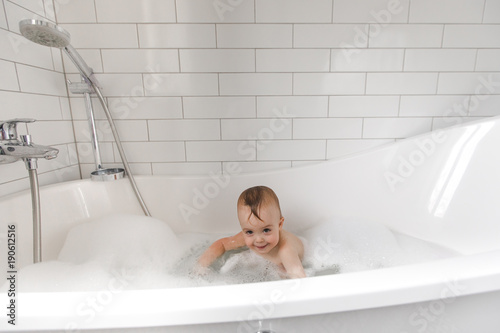 Adorable little wet boy standing and smiling in white bath.