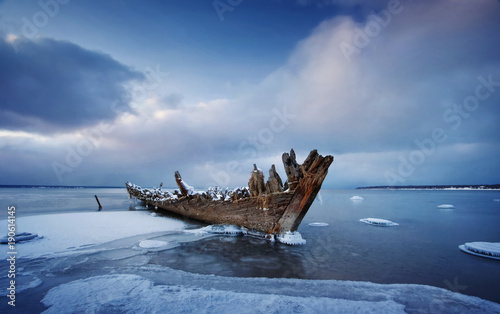 Photos Old wooden shipwreck in ice at sea. Winter on the water at night