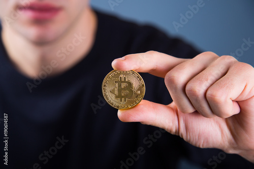 Caucasian young man holding golden bitcoin in his hand on blue background