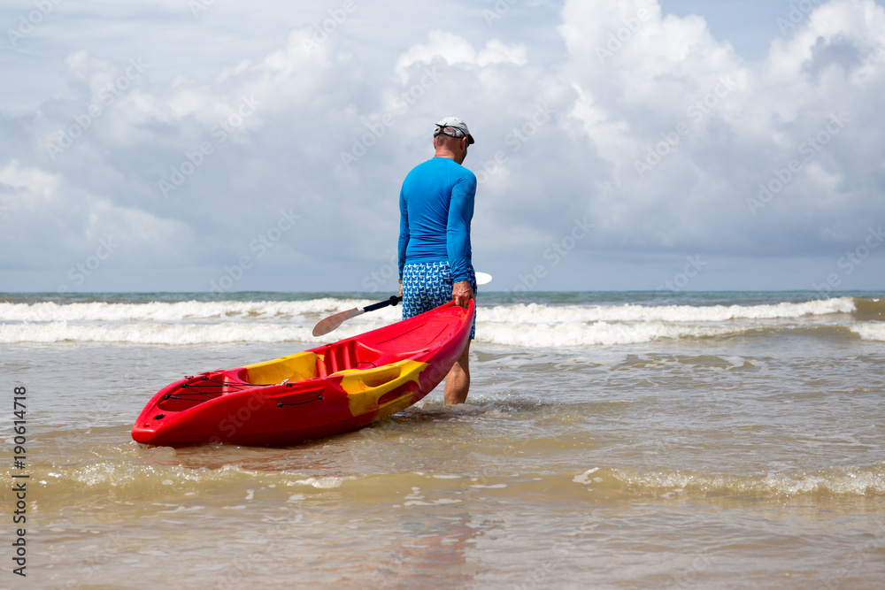 Fototapeta premium Man pulling kayak to the sea wave on vacation
