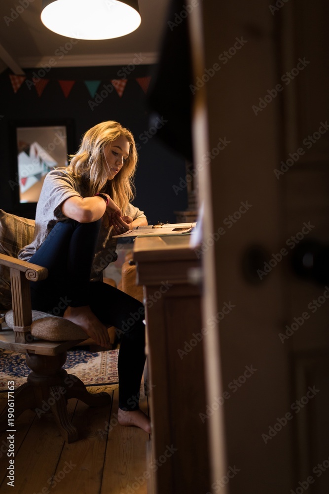 Young woman reading magazine while sitting on chair keeping one Young woman reading magazine while sitting on chair keeping one