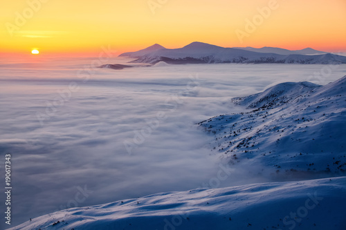 The high mountains in the fog, morning sky is enlighten with the orange colored light in winter day.