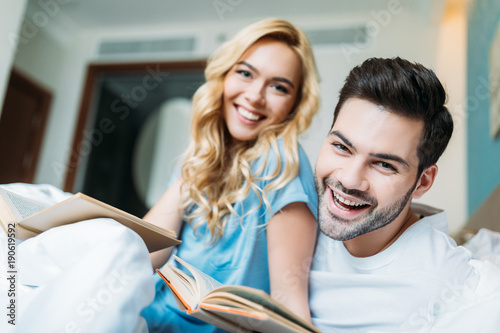 smiling couple with books in bed looking at camera