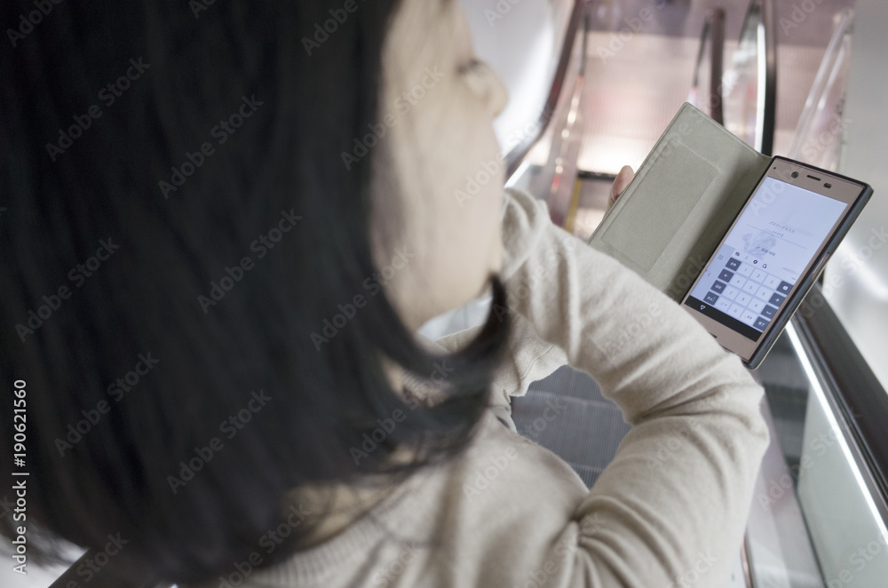 女性がエスカレータに乗ってスマートフォンを眺めている 女性がエスカレータに乗ってスマートフォンを眺めている