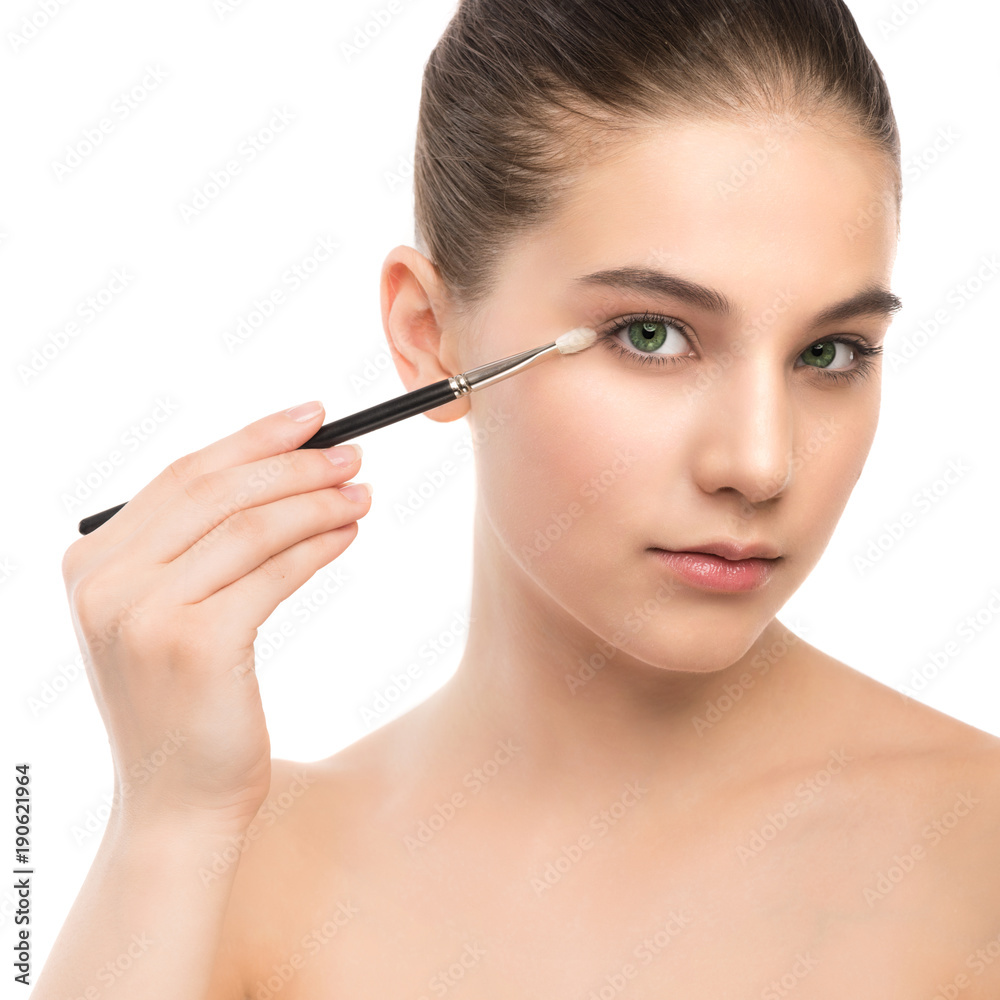 Portrait of beautiful young brunette woman with clean face. Beauty spa model girl with perfect fresh clean skin applying cosmetic brush. Youth and skin care concept. Isolated on a white background.