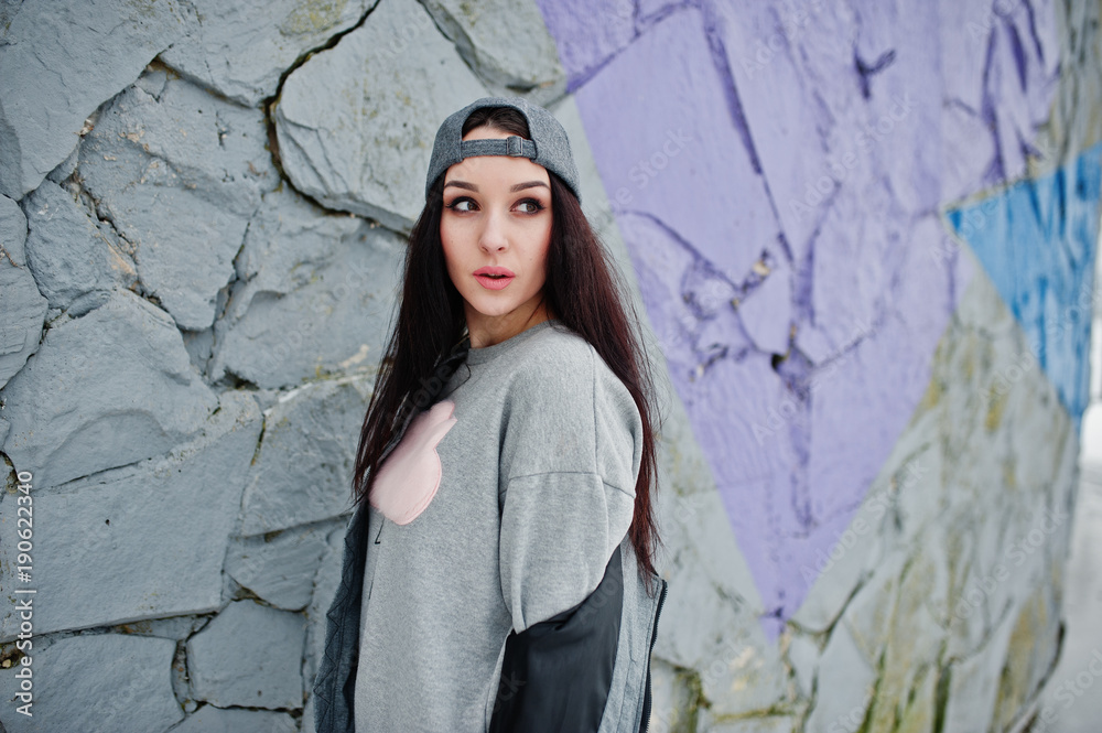 Stylish brunette girl in gray cap, casual street style on winter day against colored wall. Stylish brunette girl in gray cap, casual street style on winter day against colored wall.