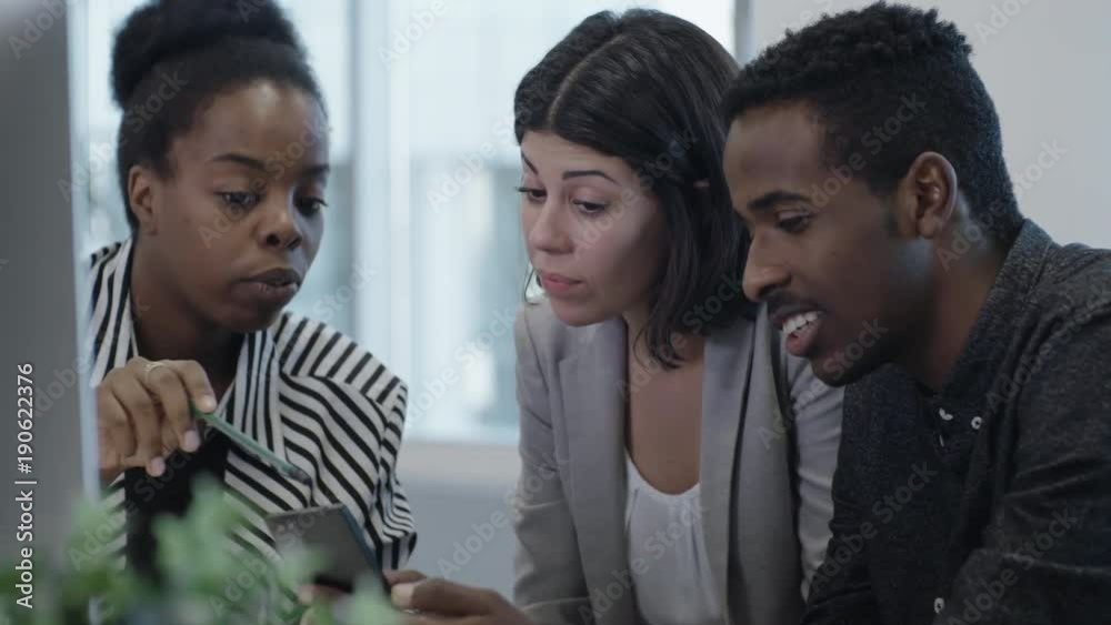 Tracking of joyful African businessman and two his female colleagues watching something on smartphone, smiling and discussing during office workday Tracking of joyful African businessman and two his female colleagues watching something on smartphone, smiling and discussing during office workday