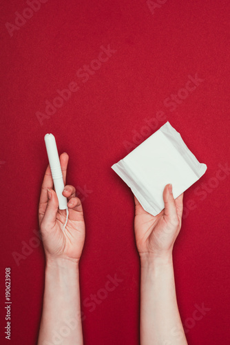 cropped shot of woman holding menstrual pad and tampon isolated on red