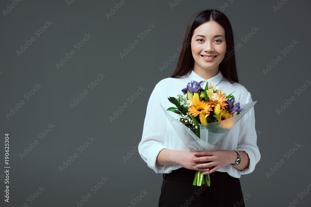 beautiful asian woman holding bouquet of flowers and smiling at camera isolated on grey beautiful asian woman holding bouquet of flowers and smiling at camera isolated on grey